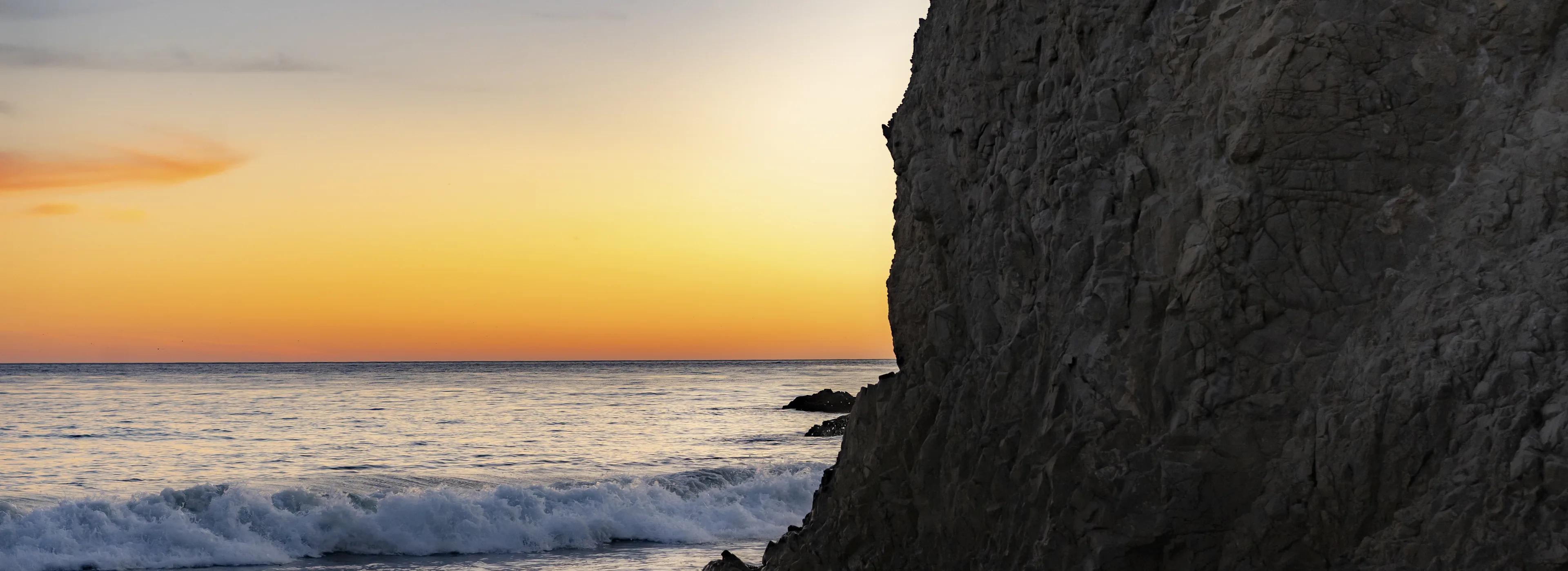 The Pacific at sunset from El Matador beach, Malibu, a dark headland filling the right of the frame