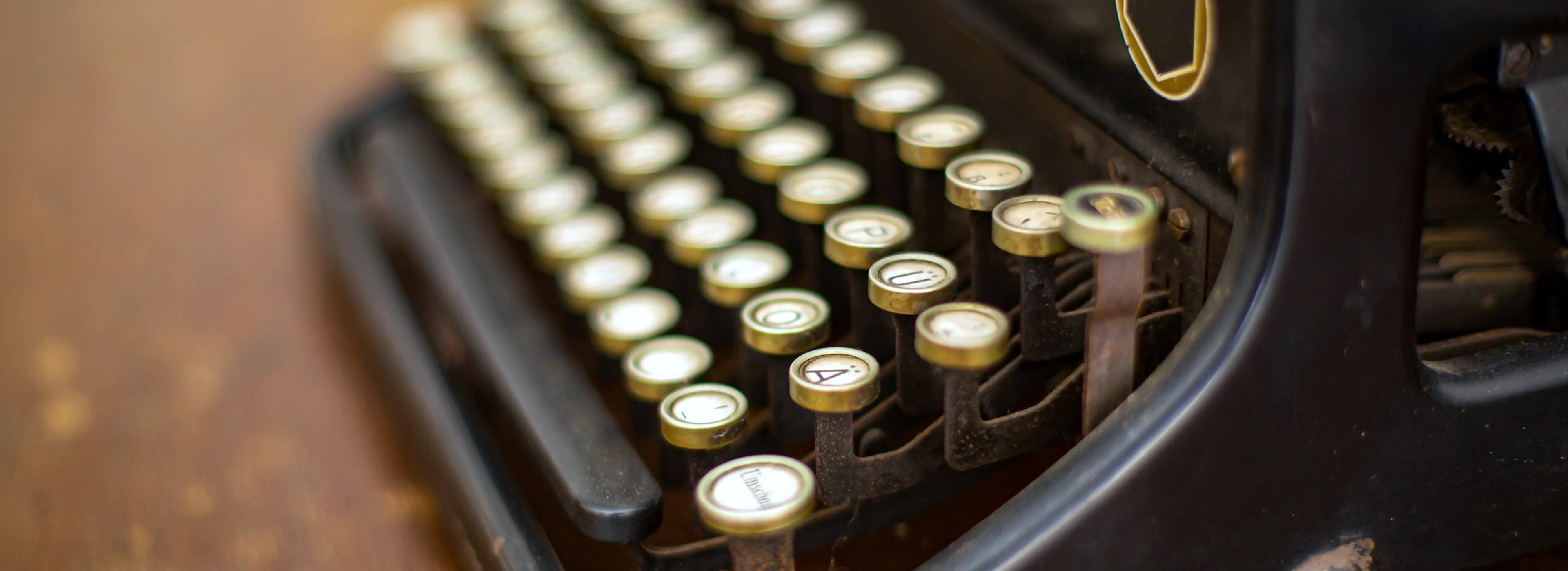 Rows of round brass-rimmed keys on an antique black typewriter, on a worn wooden desk